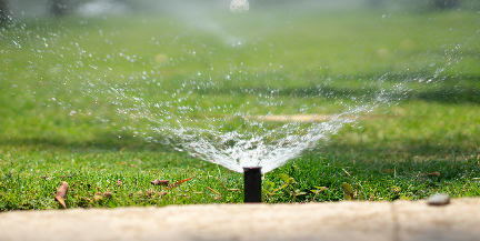 Image of a sprinkler spraying water onto a green lawn.
