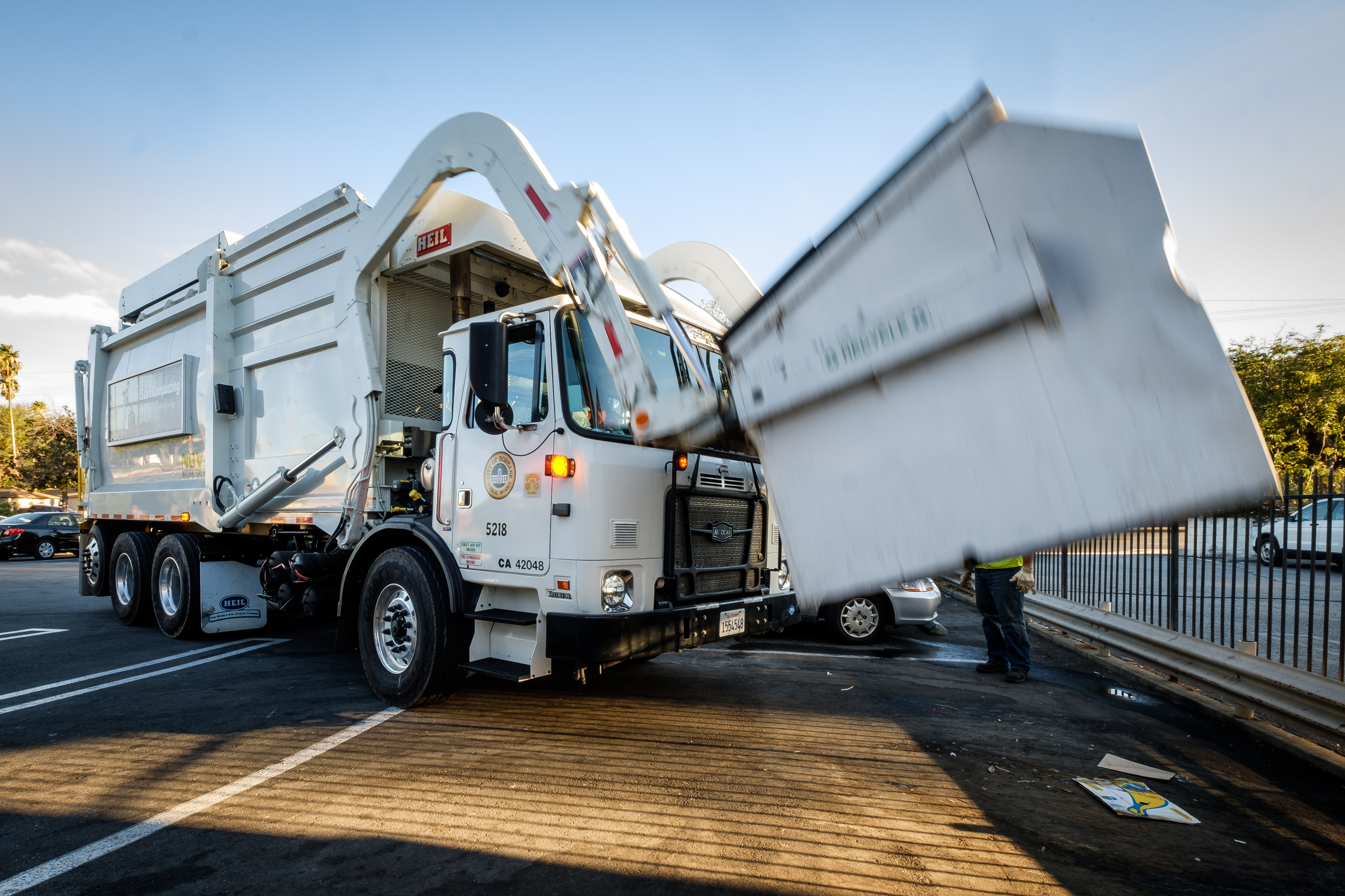 A waste collection truck using its frontloader to lift a dumpster.