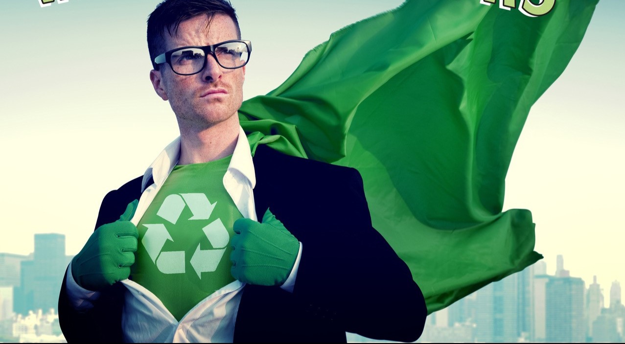 A man wearing glasses, a suit, green gloves and a green, flowing cape pulls open his dress shirt to reveal a green outfit with a recycling logo.