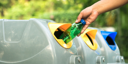 Two men in blue Public Works uniforms deposit plastic bottles into a recycle bin.