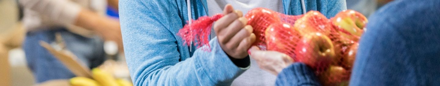 A close-up on a mesh bag of apples exchanging between two individuals.