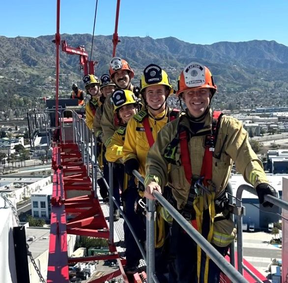 Group of firefighters smiling toward the camera on a crane wearing security equipment