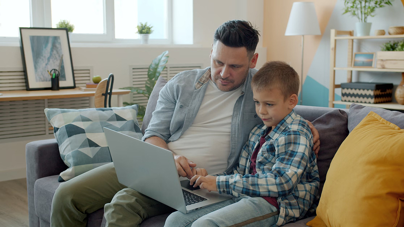 father and son using laptop on sofa