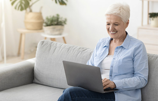 older woman sitting on sofa writing on a laptop