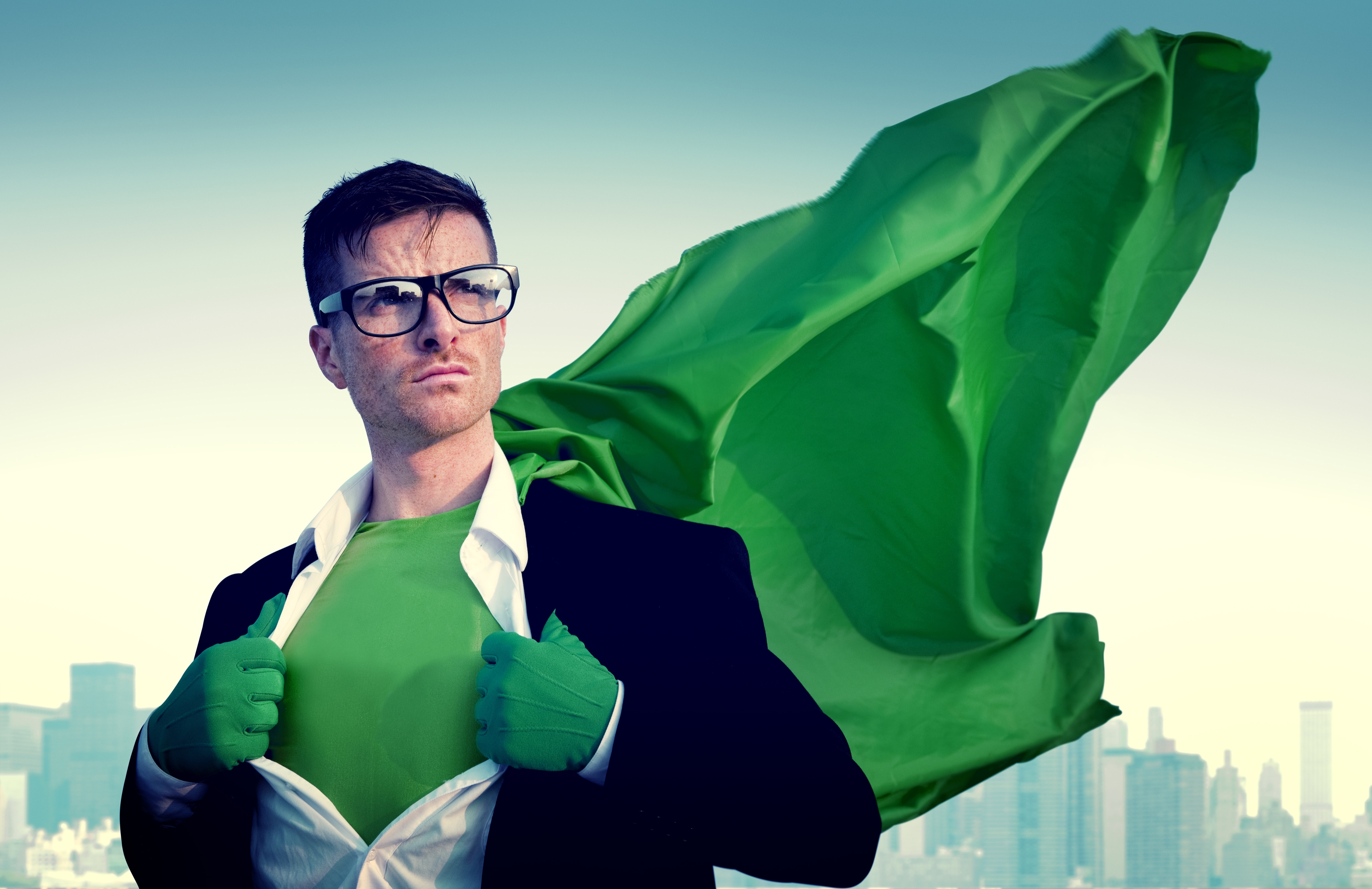 A man wearing glasses, a suit, green gloves and a green, flowing cape pulls open his dress shirt to reveal a green outfit.